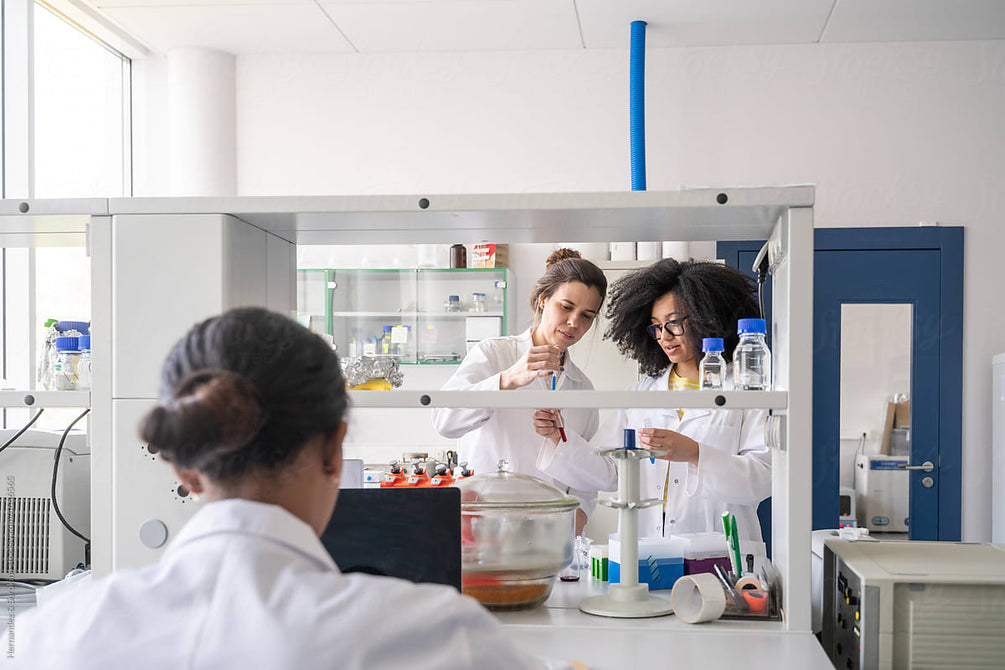 Two researchers analysing a sample together in a modern laboratory while a colleague works at a laptop